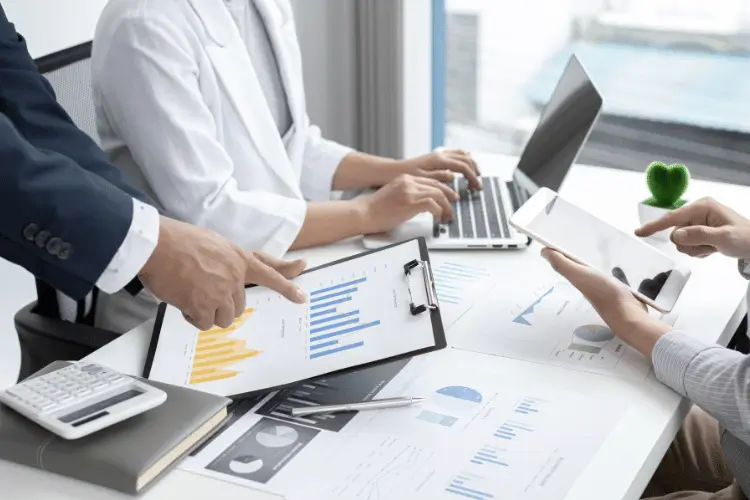 Equioe analisando gráficos crescentes no estilo de coluna. Uma mulher mexe em um notebook e um homem em um tablet